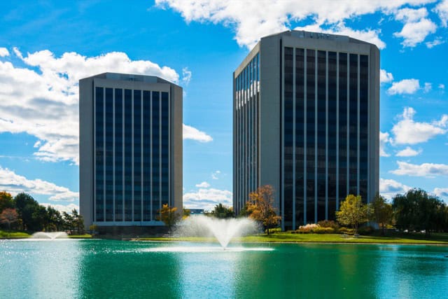 A twin-tower office complex in Dearborn, Michigan, features a pond with water fountains in the foreground.