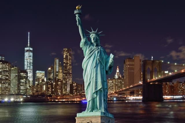 Manhattan skyline at night with the Brooklyn Bridge and the Statue of Liberty.