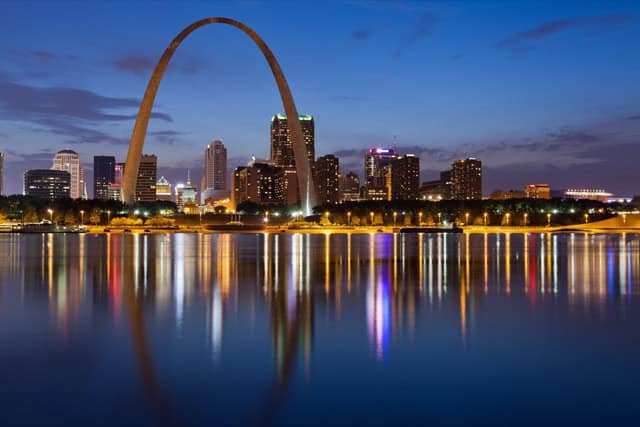 The St. Louis skyscrapers at night reflect in the river, showcasing the city's beautiful skyline.